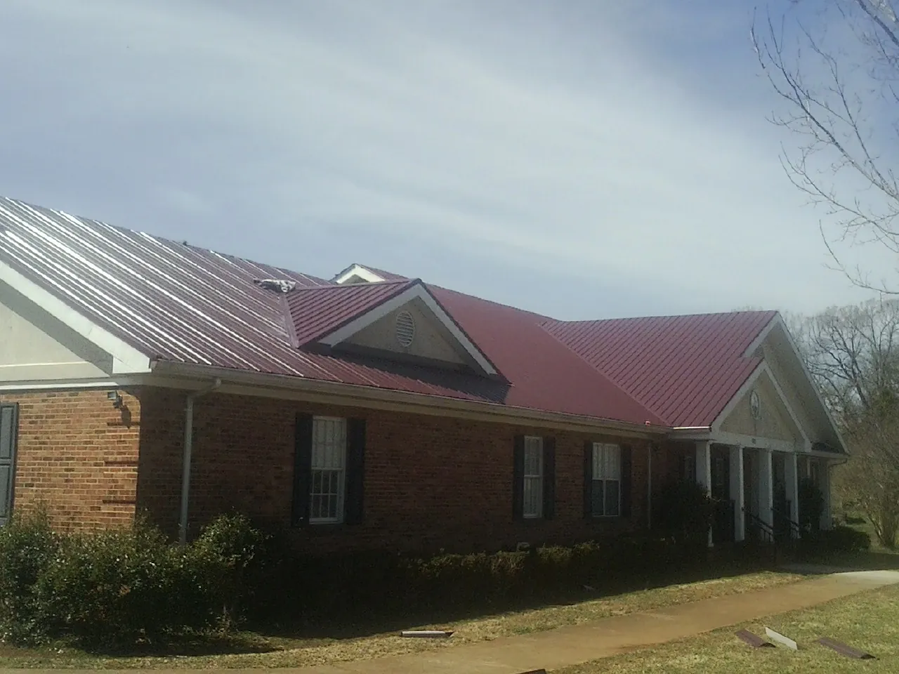 Red metal roof with gabled entries on a long brick building, from a Hail Damage Roof Repair job in Red Bank