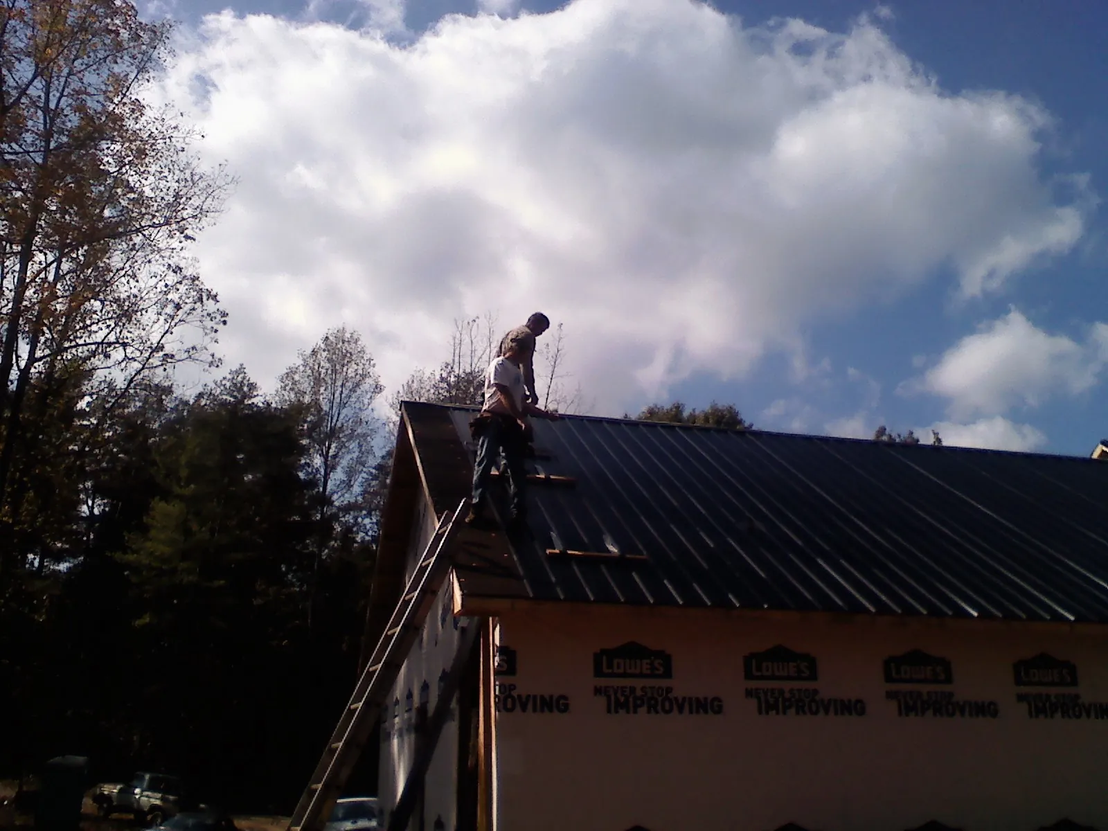Roofer fastening dark metal panels high against a cloudy sky, from a Roof Inspection job in Red Bank