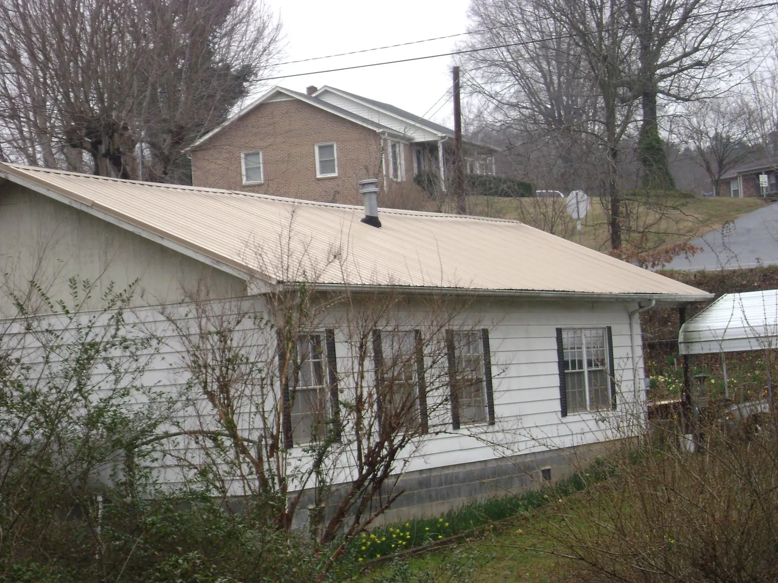 Tan metal roof on a white sided house set into a hillside — Commercial Roofing by Roofing Brothers in Red Bank